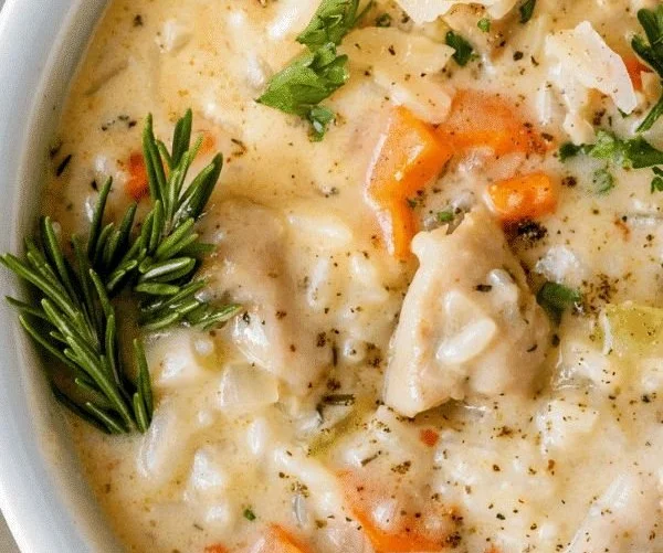 A bowl of creamy chicken and rice soup garnished with herbs