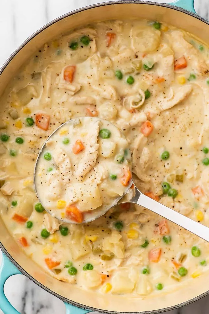 Bowl of easy chicken pot pie soup garnished with parsley, surrounded by ingredients.