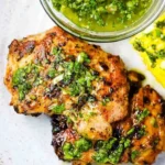 Grilled Chimichurri Chicken Thighs 3 Grilled chimichurri chicken thighs plated with fresh herbs and sauce