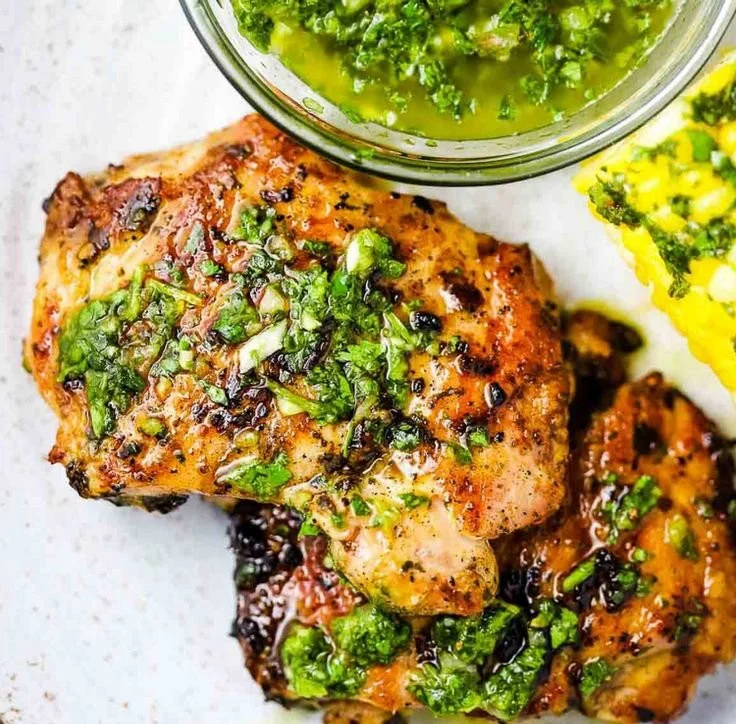 Grilled chimichurri chicken thighs plated with fresh herbs and sauce