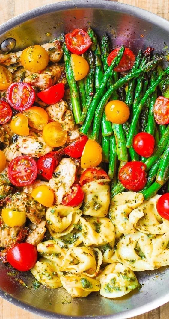 Basil pesto chicken served with tortellini, asparagus, and cherry tomatoes in a summer dinner setting