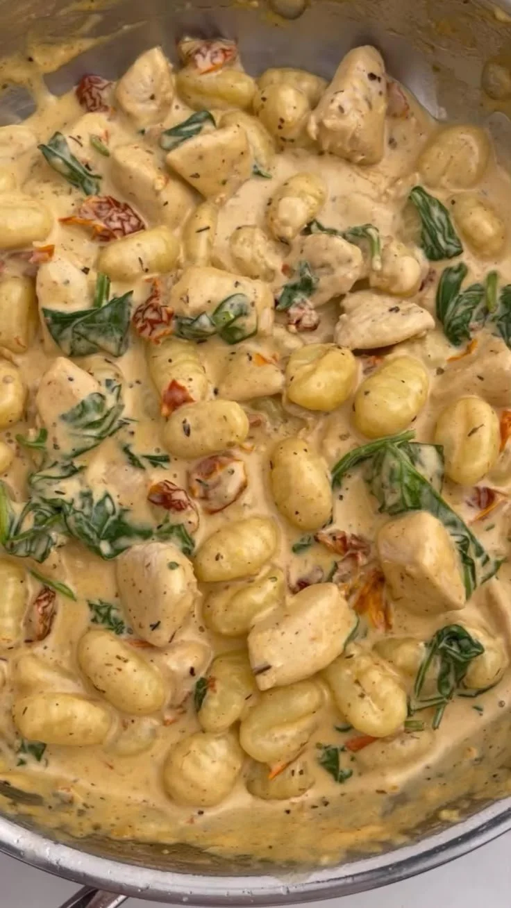 A bowl of creamy chicken and gnocchi garnished with fresh herbs.